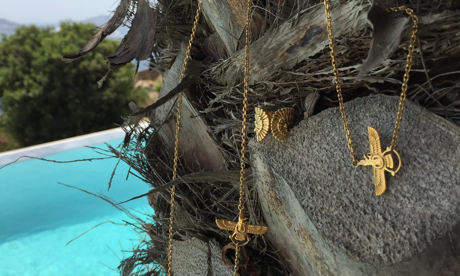 Neda Tahniat gold jewelry resting on natural stone by the sea