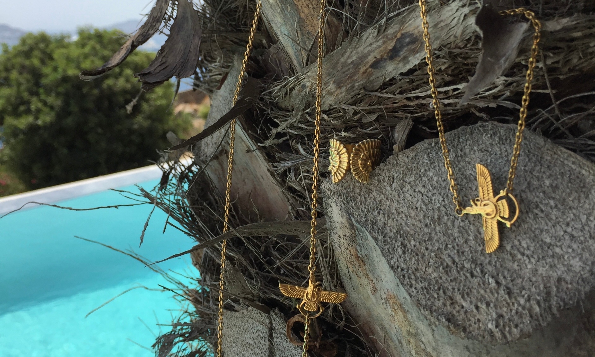 Neda Tahniat gold jewelry resting on natural stone by the sea